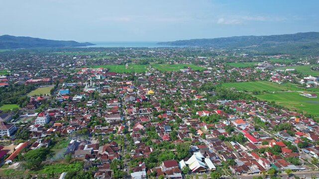 Aerial drone footage of Pacitan city from the north side, in a flat green valley, with blue sea at the horizon, in Pacitan regency, Java island, Indonesia