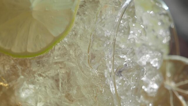 Refreshing gin tonic cocktail with ice and lime slices being poured.