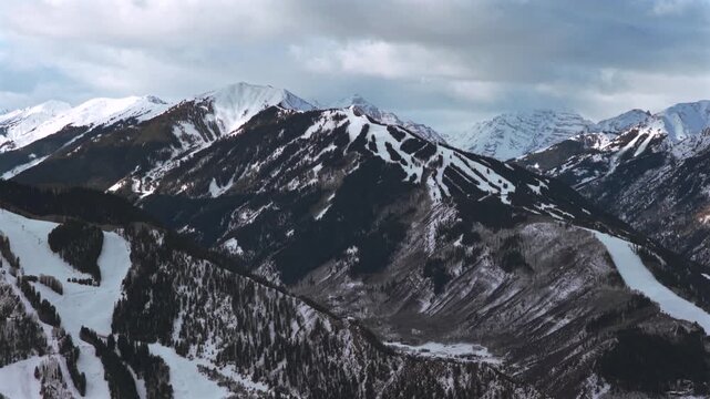 Colorado ski trail runs aerial drone Aspen Highlands Ski resort Highlands Bowl Pyramid Peak Maroon Bells Wilderness winter Aspen Mountain AJAX winter dark cloudy chairlifts pan right motion