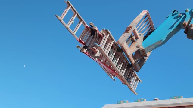 Smooth downward pan of construction lift carrying ladders above active jobsite.