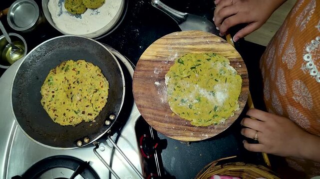 India woman preparing gujarati thepla in home kitchen, rolling dough and cooking traditional flatbread.