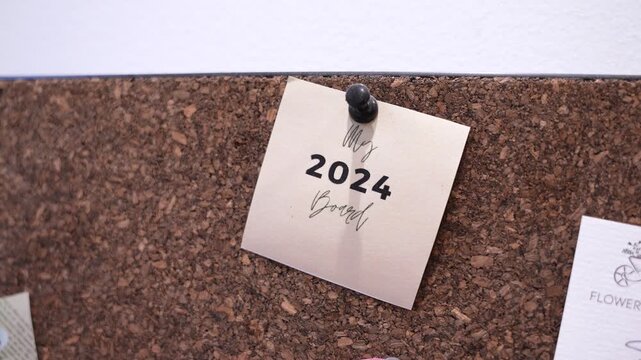 Close-up of a pinned &ldquo;My 2024 Board&rdquo; note on a cork bulletin board indoors, showing personal goal planning, organization, and motivational workspace decor with soft focus.
