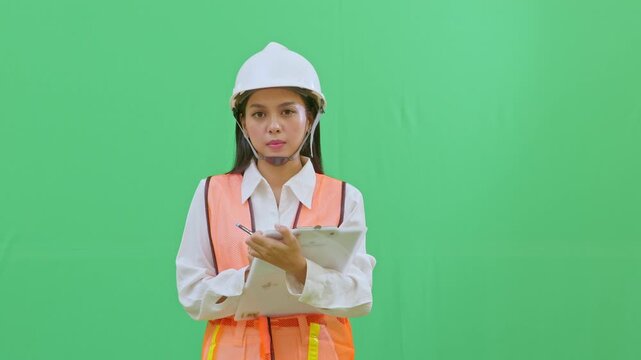 A focused female engineer in a white hard hat writing a serious safety report on a clipboard. Professional site documentation and inspection simulation on green screen.
