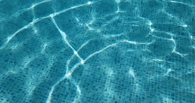 Clear blue swimming pool water with ripples reflecting sunlight and tiled floor beneath