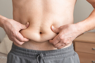 Naklejka premium Male hands pinching excess fat on the waist, symbolizing overweight, obesity, and the need for weight loss or diet. Healthy lifestyle, self-care