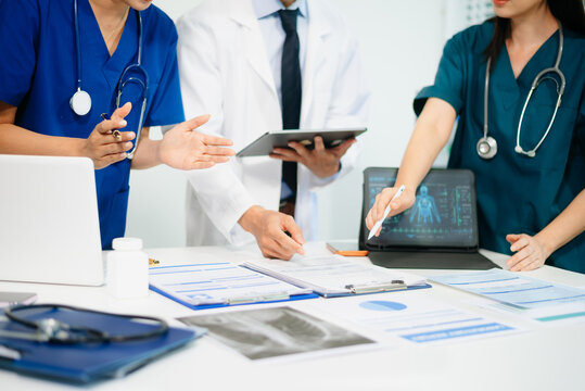 Medical team having a meeting with doctors in white lab coats and surgical scrubs seated at a table discussing a patients working online using computers