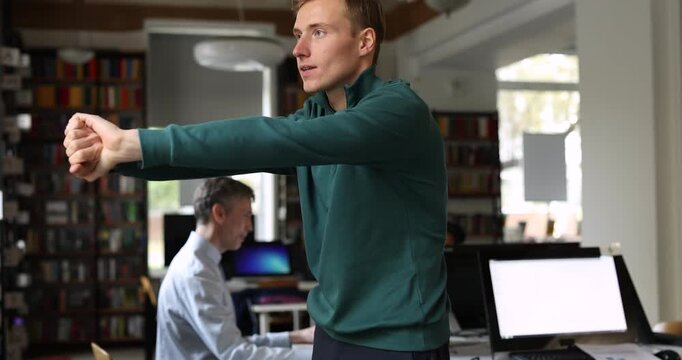 Male employee stretching body, making exercises, relieving muscle tension after long hours of computer work during break. Promoting health care, energy recovery at workplace. Office worker wellbeing