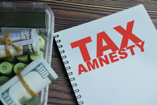 Concept of tax amnesty write on book isolated on Wooden Table. Opportunity for owe back taxes to pay some or all what they owe