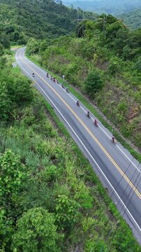 Aerial View of Cyclists on Winding Mountain Road Surrounded by Lush Greenery and Scenic Landscape