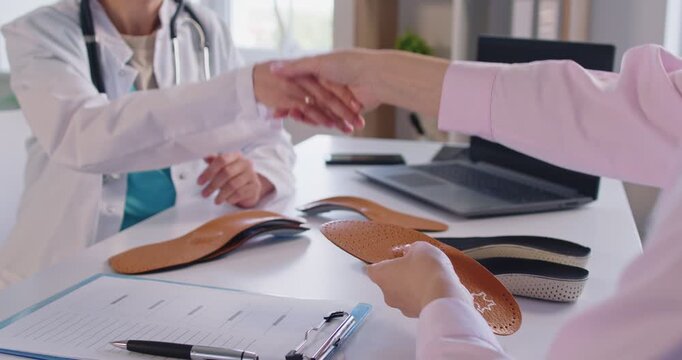 Professional orthopedist giving consultation to patient, recommending insoles for flat feet, providing orthotic care, shaking hands as sign of agreement. Feet comfort and health care concept.