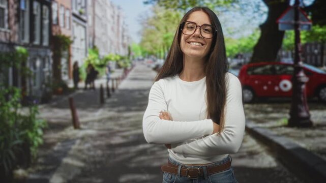 Woman giving thumbs up with visible thumb and smiling on a tree lined urban street by a red car and lamppost; optimism approval.