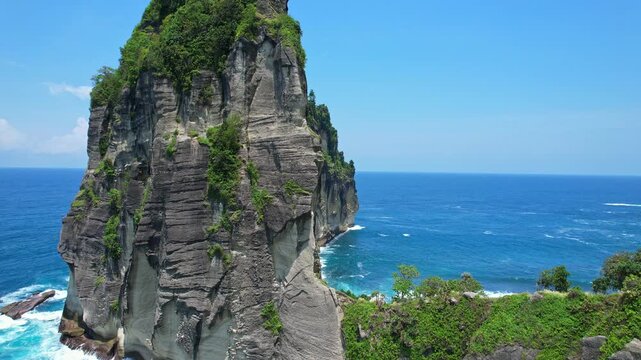 Aerial drone close up footage of Pangasan beach iconic rocky cliff nearby the blue sea, with waves, vegetation on top, in a sunny weather, in Pacitan regency, Java island, Indonesia