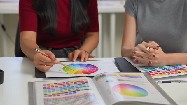 Close up of two young women hands discussing color palette and graphic design samples, creative teamwork and planning process in office..