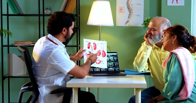 Professional Indian young male doctor explaining organ functions using a graphic figure to Asian senior retired couple patients across a table in a modern clinic; healthcare education concept.