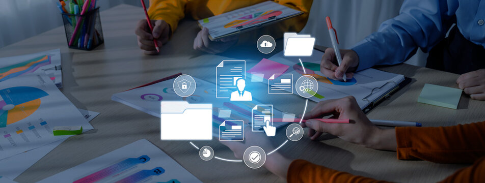 A group of people collaborates on business documents and charts at a modern office table, with digital icons representing data management and teamwork concepts. Trope