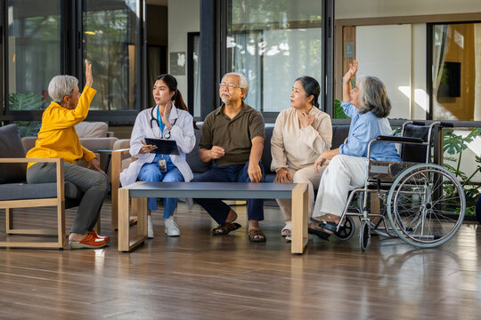 Young female doctor examining senior patient group in nursing home clinic looking happy raising hands asking question healthcare professional supporting elderly community wellbeing