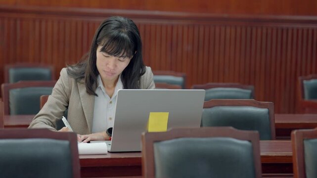 Professional female lawyer reviewing legal documents on laptop in office. Concept of law, justice, corporate legal work, and business professionalism in cinematic workplace setting.
