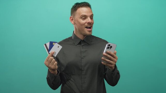 Man holding creditcards and smartphone with mouth open in studio while presenting cards and phone; financial excitement.
