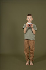 Full body of young boy holding camera and taking photo. Child photographer concept, creativity, learning and modern lifestyle in studio with neutral background. © YuliaSmyt
