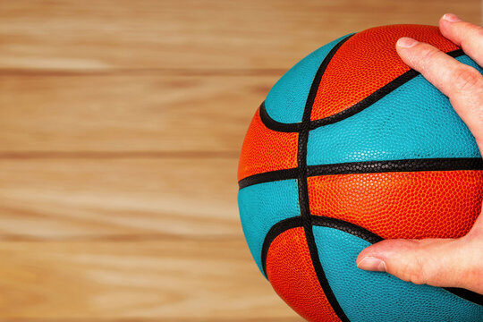 A hand grips a vibrant orange and blue basketball on a blurred w