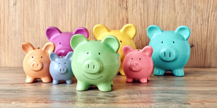 A diverse arrangement of seven colorful ceramic piggy banks in green pink yellow blue and orange on a rustic wooden surface against a light wooden bac