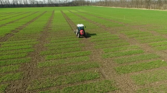 Aerial view of tractor forming separation lines across large agricultural field with multiple trial plots, highlighting organized crop research and field preparation