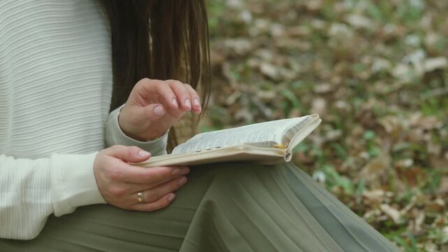 Woman in white sweater and green skirt reading a book outdoors among fallen leaves