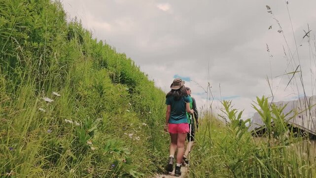 Aerial pov couple hikes together along rugged trail toward the jagged Rossz&auml;hne peaks in the Italian Dolomites. Majestic limestone peaks. UNESCO World Heritage scene. Gardena pass lope hiking trail