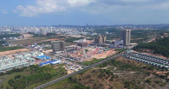Backward aerial view of Sihanoukville's urban development revealing an amusement park under construction with a Ferris wheel and roller coaster, surrounded by modern high rises 