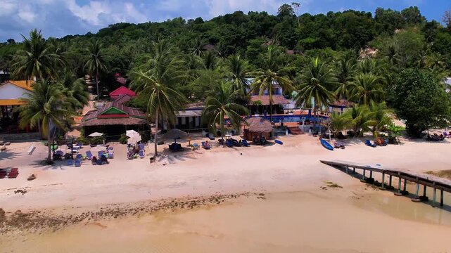 Drone footage of a tropical beach in Koh Rong, Cambodia. Featuring a paradisiac beach with white sand, turquoise waters, clear skies, and a town