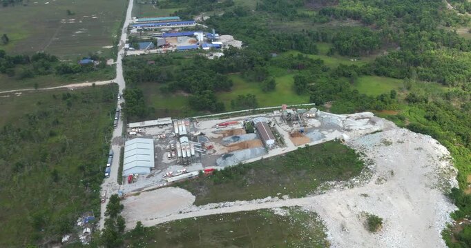 Tilt down aerial view revealing a concrete mixing plant with silos, mixer trucks, and aggregate piles surrounded by forest.