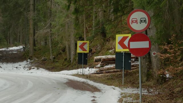 Snow covers the high-altitude mountain road, and signs indicate it is closed for winter. Drivers must turn back as they face restrictions due to weather conditions.