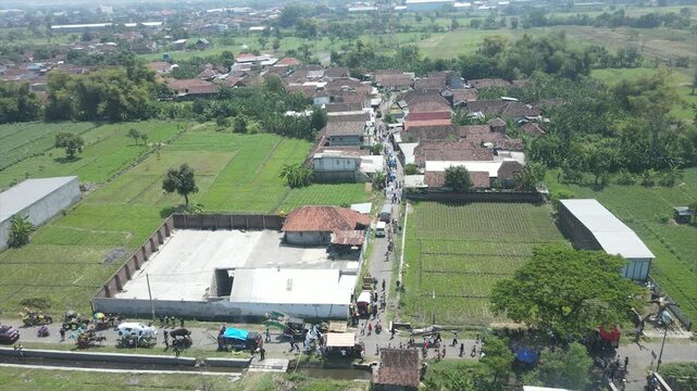 Aerial view of a local parade or funeral procession walking through a rural Indonesian village.