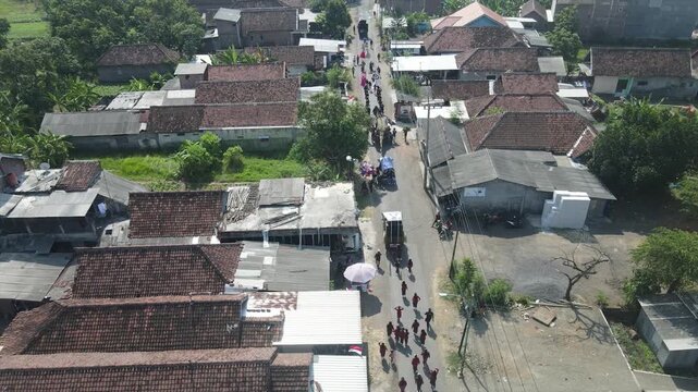 Aerial view of a local parade or funeral procession walking through a rural Indonesian village.