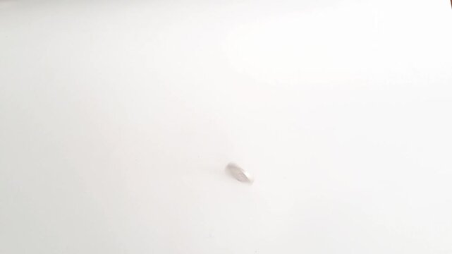 Horizontal shot of an Asian man's hands spinning a silver coin on a white minimalist background. This footage captures the concept of probability. PAMEKASAN, INDONESIA - APRIL 1, 2026