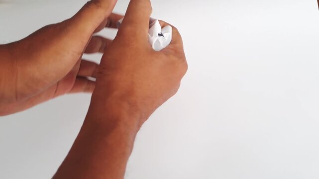 Close-up of an Asian man's hands crumpling a piece of white paper and throwing it away in anger. A minimalist horizontal shot depicting frustration, failure, creative block, and stress at work.