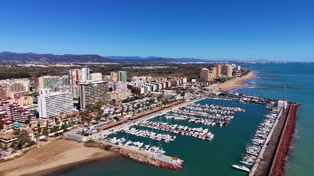 Overhead view of La Pobla de Farnals marina near Valencia, Spain, with moored yachts, turquoise water, sandy beach, and coastal apartments