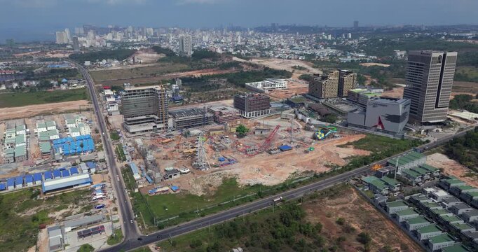 Aerial turning view of Sihanoukville's urban expansion, revealing an amusement park under construction, modern skyscrapers, and a dense city skyline.