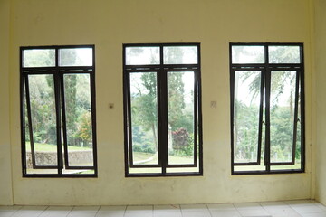 Fototapeta premium Three black-framed windows in a pale yellow room looking out to a lush green garden.