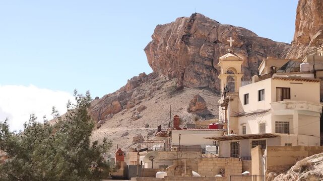 Cinematic aerial drone shot of the historic Saint Thecla Monastery built into the rocky mountainside of Ma'aloula, Syria