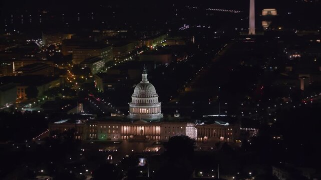 Aerial night shot of the illuminated U.S. Capitol, looking down the National Mall toward the Washington Monument amid city lights.