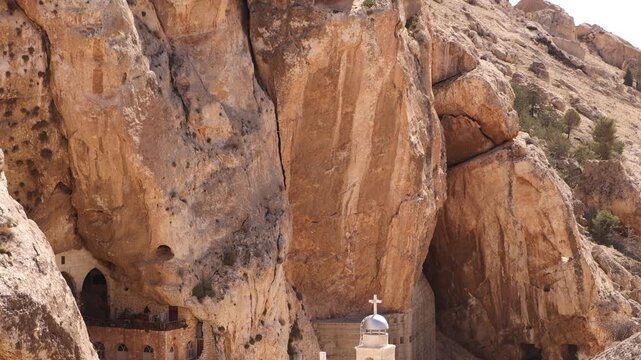Somber view of war-torn structures and rubble in Ma'aloula, featuring the historic monastery in the background