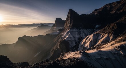 Fototapeta premium Majestic mountain range bathed in golden sunrise light, with misty valleys below.