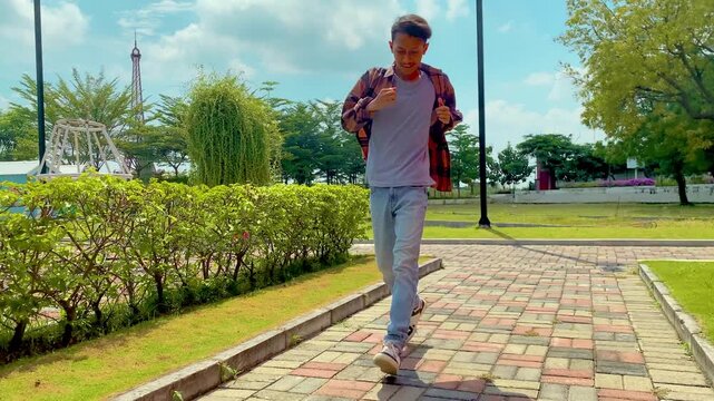 Young man walks on brick path wearing a flannel shirt at the park during daytime