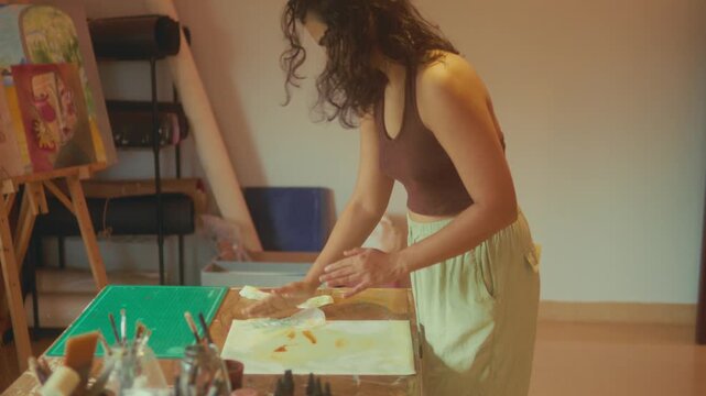 Female artist applying paint onto paper using tissue or paper for textured effect. Creative experimental technique in art studio, ideal for artistic process, craft and design concepts.