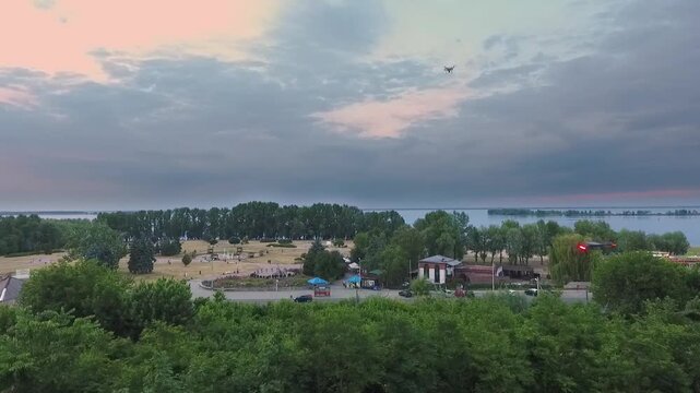 Modern Drone Flying Over Lush Green Park and Dnieper River in Cherkasy Ukraine at Sunset