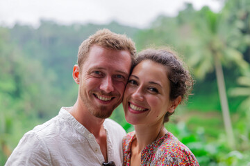 Obraz premium Close-up portrait of happy honeymoon couple embracing with lush bali jungle background, natural daylight, soft green bokeh, warm genuine smiles modern setting