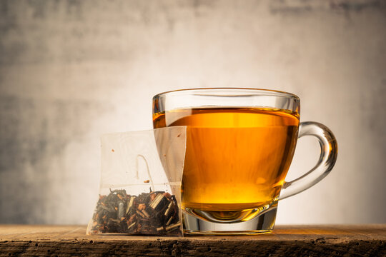 Glass cup of tea on wooden table with tea bag.