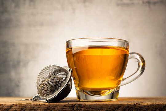 Glass cup of tea on wooden table with metal tea infuser.