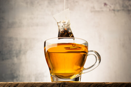 Glass cup of tea on wooden table with tea bag.
